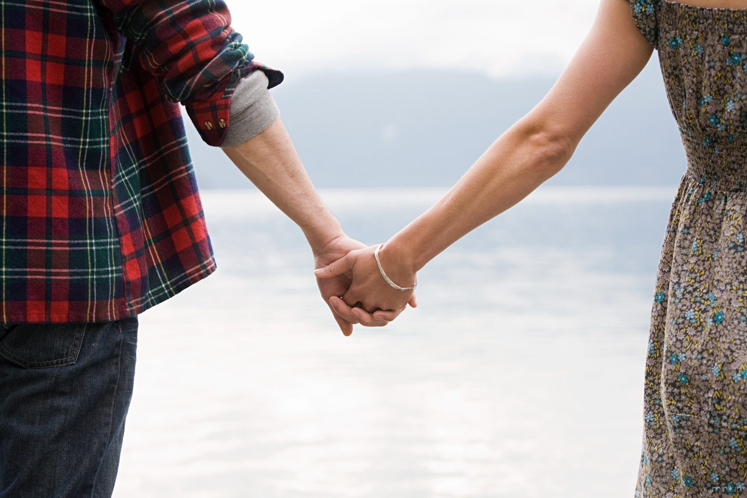 Young couple standing by lake holding hands