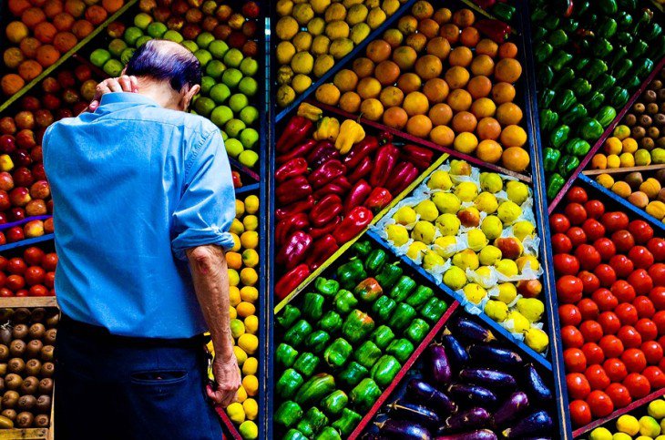 homem diante de uma prateleira cheia de frutas e legumes perfeitamente ordenado 