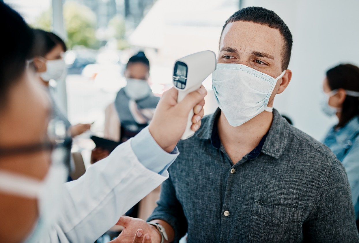 A young man wearing a face mask getting his temperature taken with an infrared thermometer by a healthcare worker during an outbreak to check for coronavirus